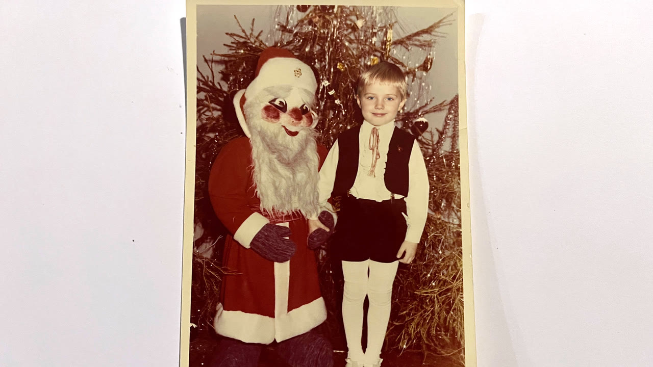 A child beside a man in a Santa Claus costume by a decorated Christmas tree